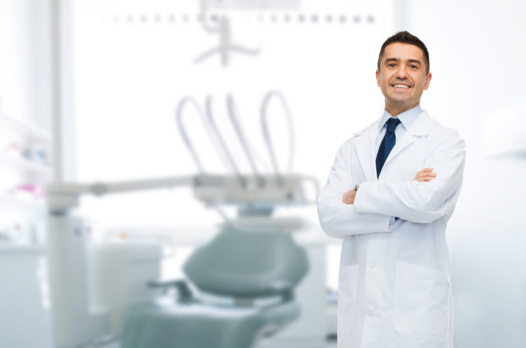 smiling male middle aged dentist over medical office background