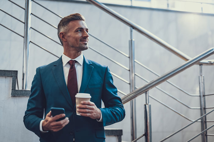 Businessman holding his phone and having a cup of coffee